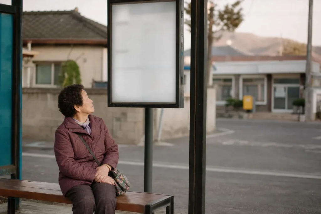 경로우대 교통카드 동네 버스 정류장 의자에 앉아 시간표를 올려다보는 노년 여성. (Elderly Korean woman sitting at a neighborhood bus stop looking up at the timetable)